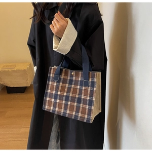 Close-up of blue and brown plaid canvas tote bag with woven handles and golden clasp