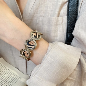 Close-up of a leopard print round link bracelet with gold-tone twisted rope edges on wrist