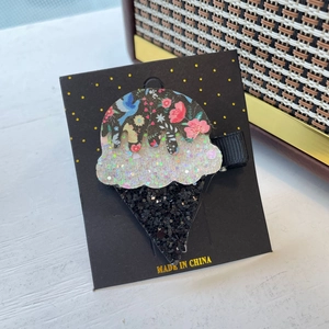 Detail of glittery ice cream hair clip on black card with colorful floral pattern and sparkles