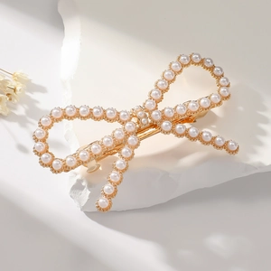 Close-up of elegant gold bow hair clip with white pearls on white stone base
