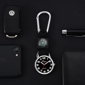 Silver clip-on watch with black dial and compass shown next to everyday essentials