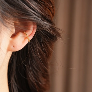 Detailed close-up of 18k gold-plated cuff earring with micro-bead texture on model's ear
