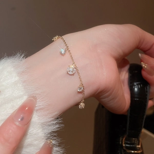 Detail of a gold bracelet with zircon Saturn and flower charms on a woman's wrist