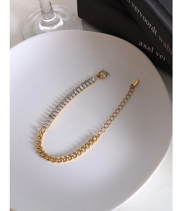 Detailed macro of 18k gold chain bracelet featuring rectangular zircon stones and logo tag