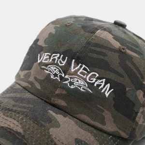 Detail of Very Vegan embroidery and crow logo on washed camo baseball cap texture