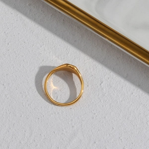 Detailed view of a polished gold sunflower signet ring on a textured white surface