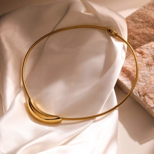 Gold minimalist snake chain necklace with a curved polished metal pendant on silk background