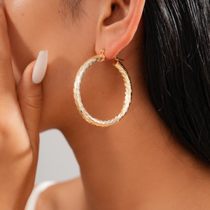 Close-up of gold geometric twisted hoop earrings with a textured spiral finish on model