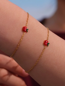 Dettaglio di un braccialetto dorato per bambini con ciondoli a mela in smalto rosso al polso