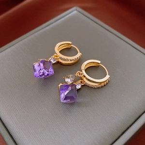 Close-up of golden hoop earrings with purple cubic pendant on a grey jewelry box