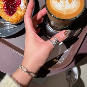Macro shot of 925 silver link chain bracelet and hollow logo ring in a coffee shop setting