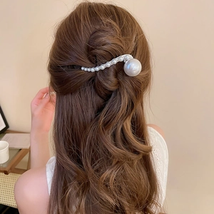 Elegant pearl hair clip with S-shaped curve design on long brown hair detail view