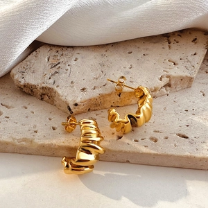 Detail of 18k gold croissant hoop earrings with ribbed texture on travertine stone