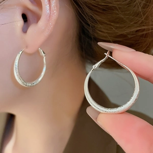 Détail macro d'une boucle d'oreille argentée mate avec texture givrée et pendentif rond