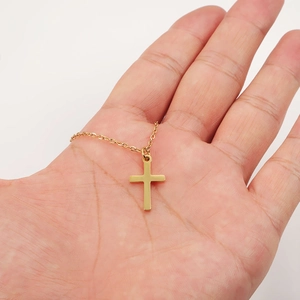 Men's minimalist gold cross pendant necklace in stainless steel shown on a hand palm