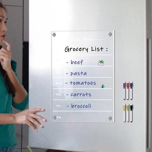 Close-up of magnetic acrylic weekly planner on fridge with colorful markers and grocery list