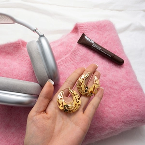 Détail de boucles d'oreilles dorées vintage en dentelle ajourée, tenues par la main
