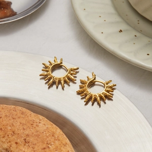 Detail of 18K gold stainless steel sunburst hoop earrings on a metal tray
