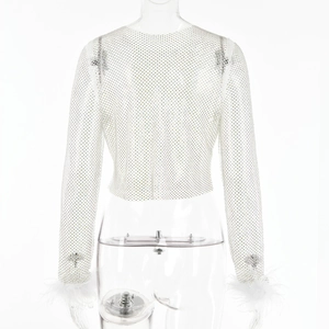 Détail d'un haut en maille blanche avec strass scintillants et poignets en plumes blanches