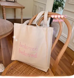 Detail of the beige canvas tote bag featuring pink gradient 'beloved' embroidery