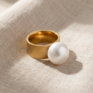 Macro detail of wide golden brushed steel ring featuring a large round white pearl inlay