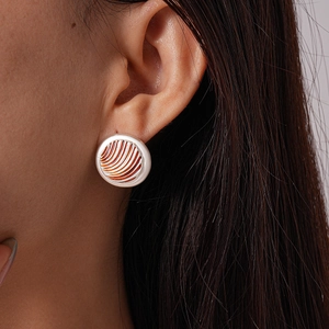 Close-up of geometric striped enamel earrings in orange and silver on model ear
