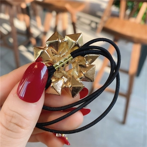 Macro view of a black elastic hair tie featuring a geometric gold faceted metal ornament
