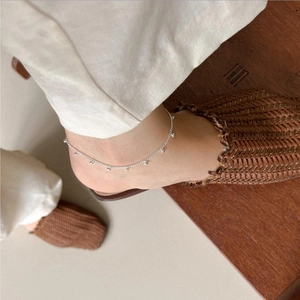Detail of a silver beaded anklet on an ankle with woven shoes and casual wood background