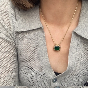 Close-up of golden snake chain necklace with square emerald green gemstone pendant