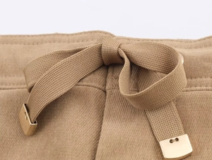 Gros plan détaillé de la taille d'un pantalon kaki avec cordon et embouts en métal doré