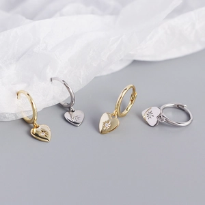 Macro shot of gold and silver heart hoop earrings with star-set zircon on grey background
