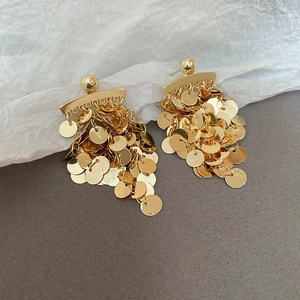 Macro shot of gold layered disc tassel earrings on textured white paper and grey backdrop
