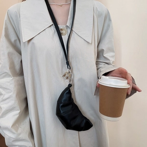 Mini sac collier noir en forme de croissant porté sur un trench-coat beige élégant