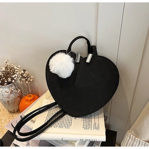 Detail der schwarzen herzförmigen Tasche mit weißem Plüschball und silbernem Reißverschluss