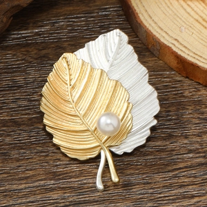 Elegant gold and silver leaf brooch with textured veins and a white pearl on wood