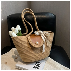 Close-up of woven straw tote with leather flap, lace bow, and pearl buckle detail