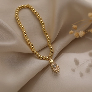 Gold beaded bracelet with girl pendant and heart zircon on cream silk background