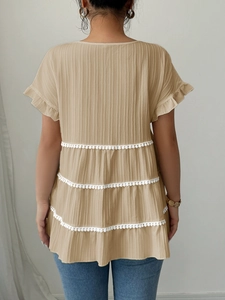 Detailed back view of beige textured blouse featuring tiered ruffles and white pom-pom trim