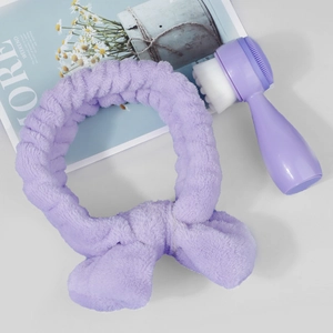 Macro detail of purple bow plush headband and double-sided silicone facial cleansing brush