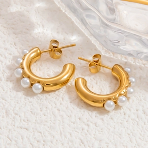 Detail of gold C-shaped earrings with white pearls on a minimalist textured surface