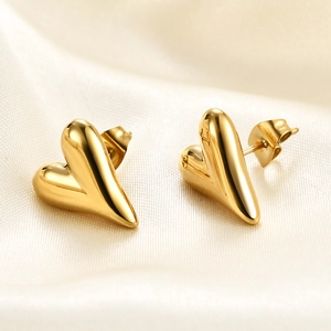 Detailed close-up of golden polished heart earrings resting on soft beige silk fabric