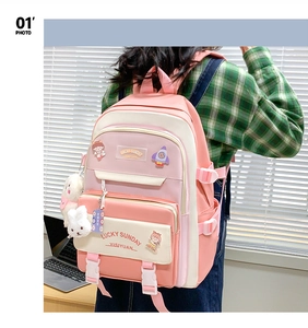 Pink and cream student backpack with cartoon pins and plush rabbit pendant in a room