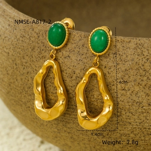 Macro shot of geometric gold earrings with green oval stone hung on textured bowl
