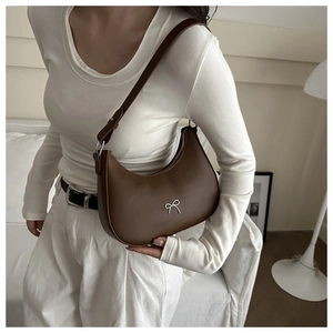 Detail view of brown crescent handbag with a silver bow ornament held by a model