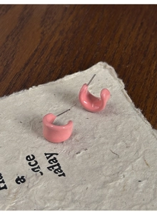 Close-up of pink C-shaped resin earrings with a glossy glaze on a rustic paper background