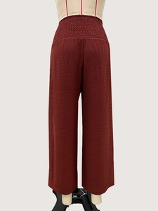 Détail de la taille haute élastiquée à plis sur un pantalon large texturé rouge foncé