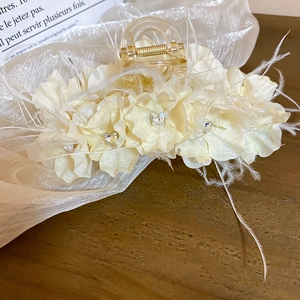 Vue détaillée de la pince à cheveux avec fleurs en mousseline, cristaux et plumes blanches