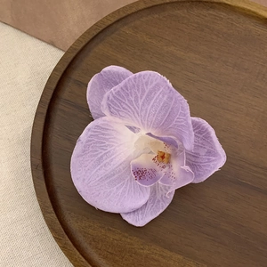 Detailed view of realistic purple orchid hair clip on a dark wooden plate with clear textures