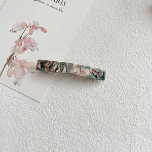 Macro shot of green and beige marbled acetate hair clip on a textured white surface