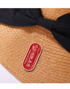 Detail of red enamel inspirational brooch with gold text pinned on a woven straw hat